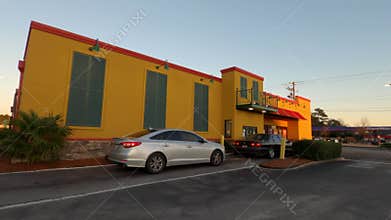 Pan of Popeyes fried chicken restaurant drive thru line people in cars waiting golden hour