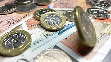 Two British pounds coin spinning on a pile of pound sterling bank notes. UK financial system. British pound, world currenc