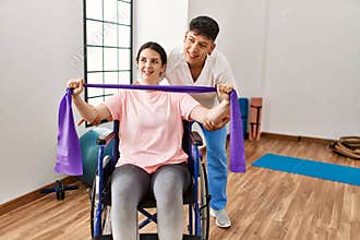 Young disabled woman sitting on wheelchair making mobility exercise using elastic band at the clinic