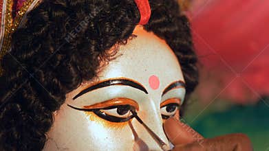 Closeup shot of a craftsman`s hand painting eyes of Goddess Durga`s clay
