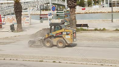 Bobcat with sweeping device cleaning street before laying new asphalt surface. Local road repair near marina. Street in