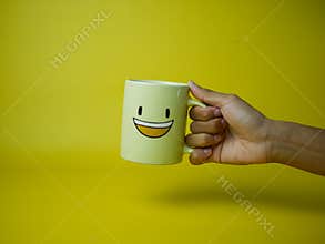 hand holding yellow coffee mug with smile emoticon icon.
