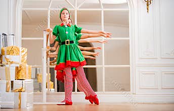 Children dressed in costumes of Christmas elves practice at a ballet bar in front of a mirror in a spacious white studio