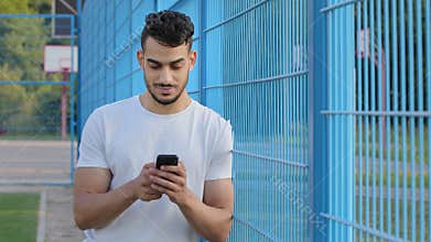 Middle eastern indian man holding phone in hands texting message or using mobile apps, checking social media