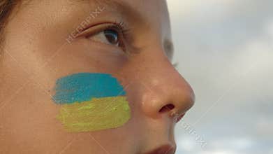 Portrait of a refugee boy from Ukraine. Flag of Ukraine on the face. Children of war in Ukraine. War refugee concept