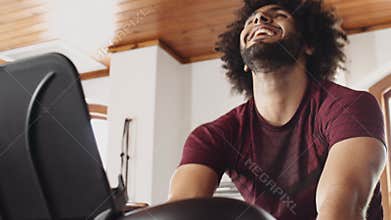 Young adult Middle Eastern male celebrating while cycling on indoor fitness bike, happy and fit in an indoor fitness gym