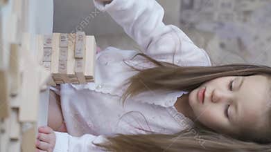 Cute curious little girl builds tower of wooden blocks.