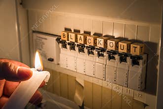 Fuse box with fuses in a distribution box during a power outage lit with white candle holding a man with the word blackout as text