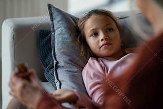 Grandmother taking care of her ill grandchild lying on sofa