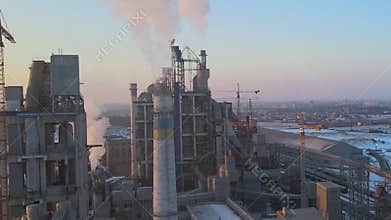 Aerial view of cement plant production area with high concrete factory structure and tower cranes at industrial site