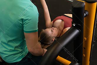 Instructor led training helps a beautiful client to perform exercises in a fitness club, the concept of playing sports