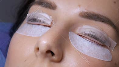 Face of a young girl on a modern eyelash lamination procedure in beauty salon. The master applied special silicone