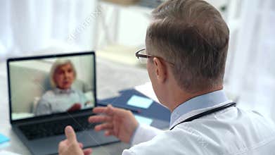 Online consultation. Middle aged doctor consulting an elderly patient woman via the internet, using laptop and sitting