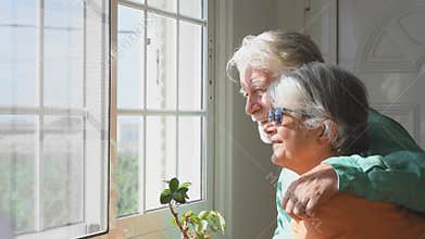 Couple of two cute old and mature people or seniors having fun together at home looking outside of their house smiling and laughin