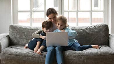 Smiling affectionate young mother watching cartoons on computer with kids.
