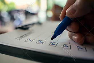 Hand with blue pen marking on checklist box