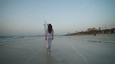 Female tourist walking on the beach in Dubai in front of Burj Al Arab