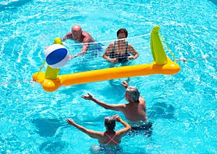 Above view of four senior people playing volleyball in the pool water. Blue color under the sun. Transparent water. Smiles and