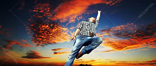 Man jumping out of happiness and emotions in front of a dramatic cloudy sunset