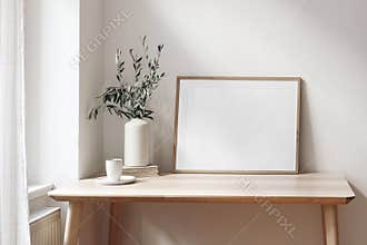 Home office concept. Empty horizontal wooden picture frame mockup. Cup of coffee on wooden table. White wall background