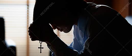 Asian man bowing his head on the Bible and carrying a cross. According to the beliefs of Christianity Is the salvation of Jesus.