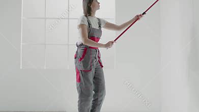 Young woman builder paints wall with roller in apartment