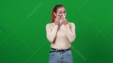 Young emotional Caucasian woman crying wiping tears with tissue. Portrait of young lady on green screen expressing
