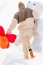 Young man from behind hugs holding big teddy bear soft toy gift heart air balloons on this special day surprising girlfriend. roma