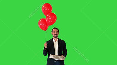 Handsome guy in an elegant suit with a gift box and balloons walking on a Green Screen, Chroma Key.
