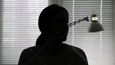 Hidden identity, unknown person, silhouette, interview. Dark female silhouette on background of light from window