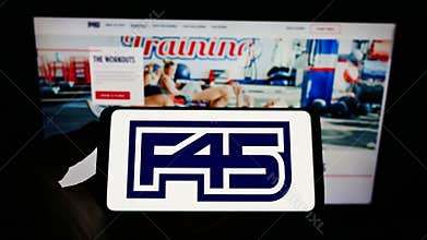 Person holding cellphone with logo of fitness company F45 Training Holdings Inc. on screen in front of business webpage.