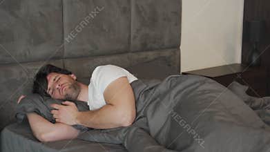 Insomniac young man cannot fall asleep, due to an uncomfortable pillow, suffering from insomnia with stress and sleep