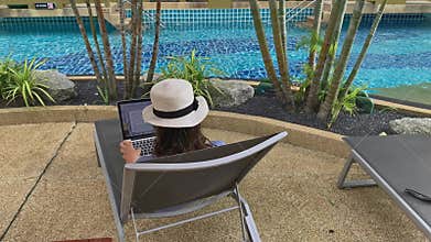 Business woman working on laptop computer near exotic tropical swimming pool. Female freelancer