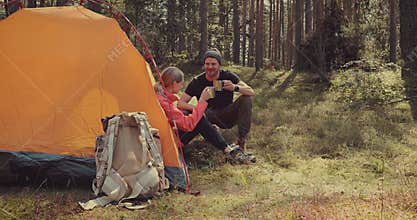 Camping trip - young couple resting by a tent at forest camp after hike. active travel