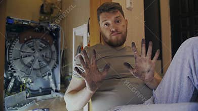 Middle-aged man shows dirty hands after repairing washing machine