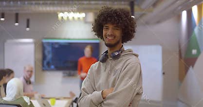 African American man, donning headphones, strikes a pose for a videographer, while his friends lead a dynamic meeting in