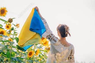 Young ukrainian woman waving national flag on sunflowers, wheat field background