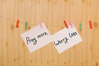 Pray more worry less - christian lettering on wooden background, card with text on rope and colorful clothespin