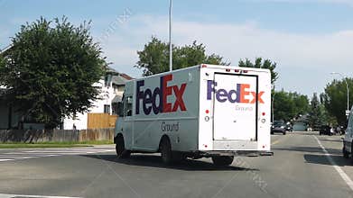 A white FedEx Ground delivery truck driving on a residential street.