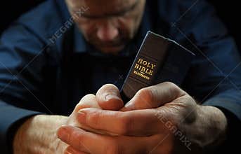 A Man praying holding a Bible.