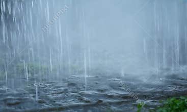 Heavy rain pours down on a surface, creating ripples and splashes as water accumulates, symbolizing a downpour and