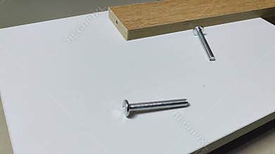 A man\'s hand places a set of three flat screws on top of the white board and one of the screws is falling down.