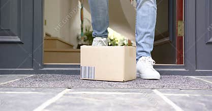 Low section of biracial man picking up delivery in cardboard box outside front door, slow motion
