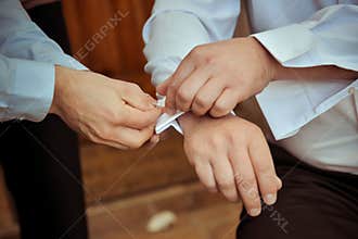 Groomsman helping the groom with his cuff buttons