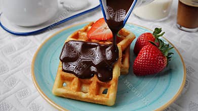 Liquid dark chocolate sauce is poured on belgian waffles. Sweet breakfast strawberry coffee milk.