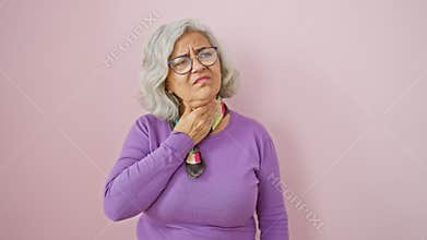 Grey-haired middle age woman, standing in pain, touching sore neck over pink isolated background, aching throat hinting to flu,