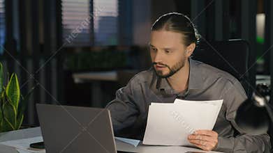 Caucasian business man at evening office work papers check documents report data information typing laptop computer