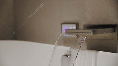 Close-up water from the tap fills into the white modern bath. Empty bathroom. Modern luxury and cozy bathroom slow