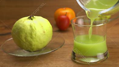Pouring fresh green guava juice into transparent glass.