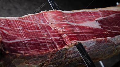 Knife cutting slicing a traditional Iberico Spanish ham, jamon. Whole leg. Close up